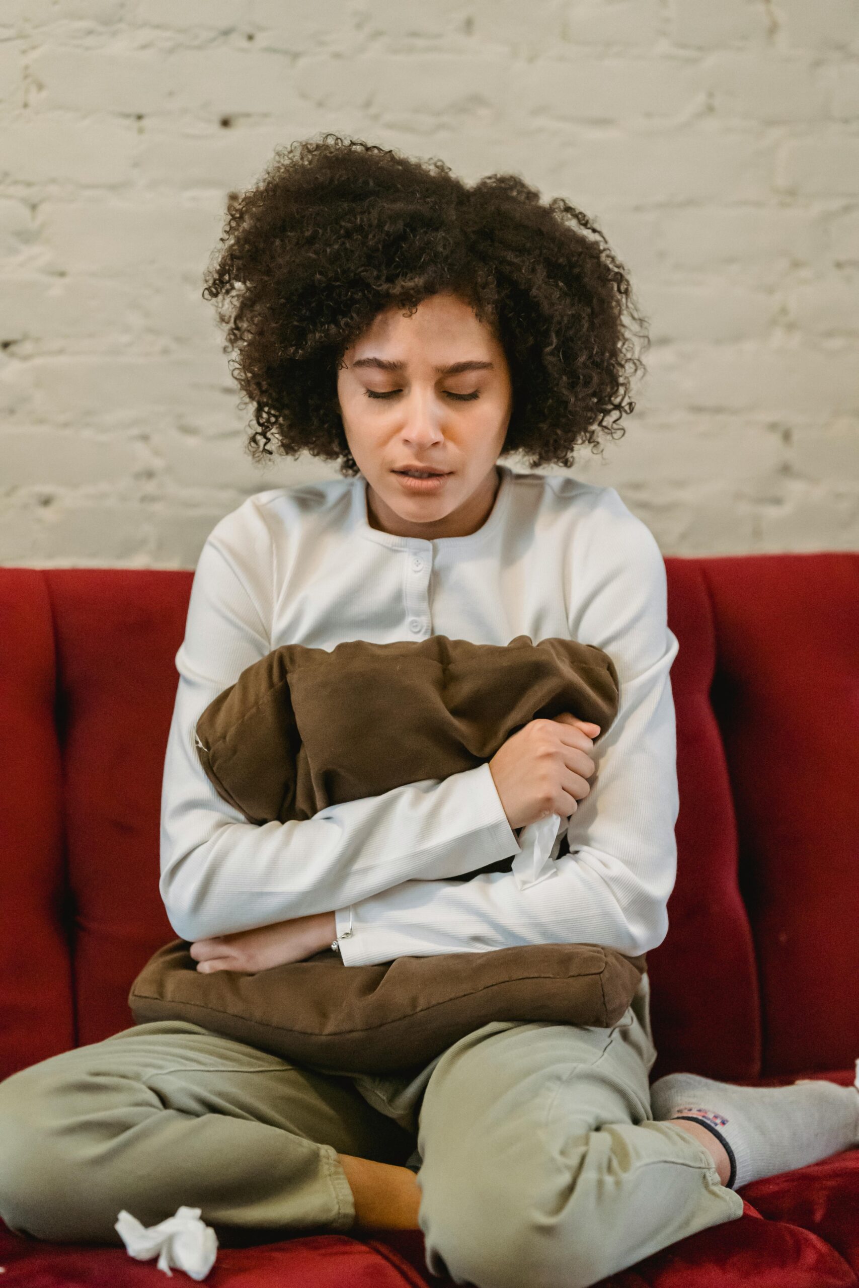 Crying young black lady embracing cushion on couch